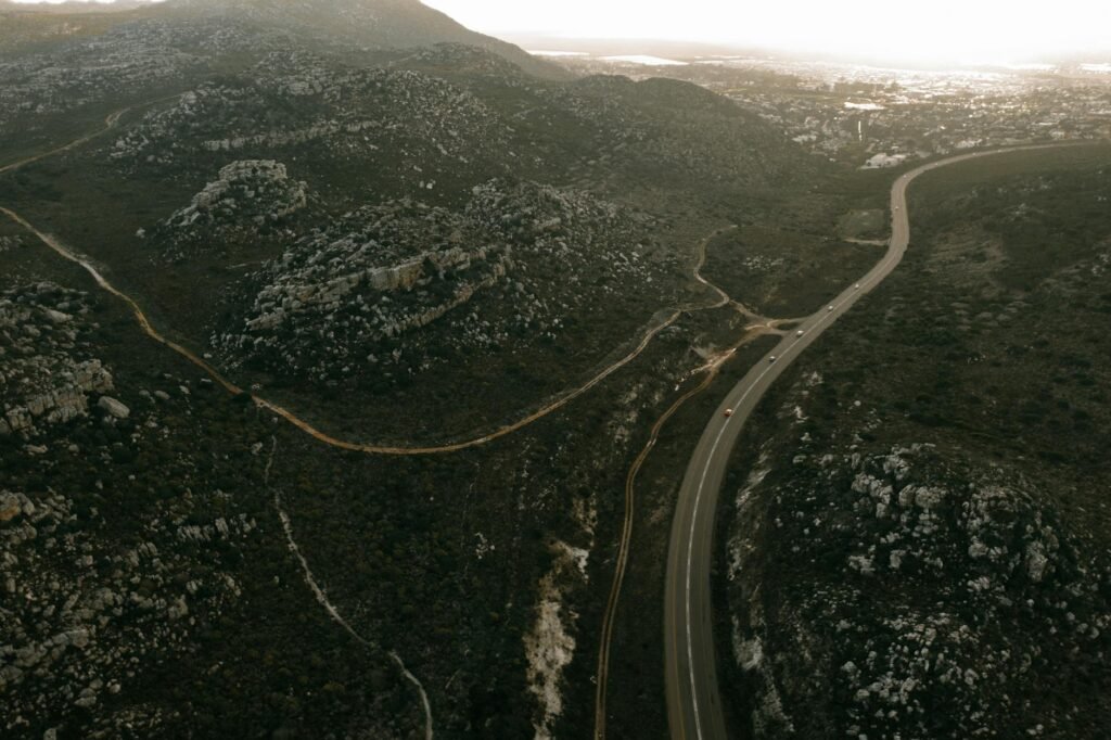 A scenic aerial view of a winding road through rugged hills at sunset, showcasing natural beauty and travel allure.