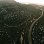 A scenic aerial view of a winding road through rugged hills at sunset, showcasing natural beauty and travel allure.
