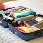 Open suitcase with camera, clothes, and passport, ready for a summer vacation.