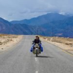 A solitary biker traveling through the rugged terrain of Leh, surrounded by majestic mountains.